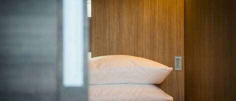 A narrow, wooden-paneled room with a bed featuring white and orange checkered bedding.