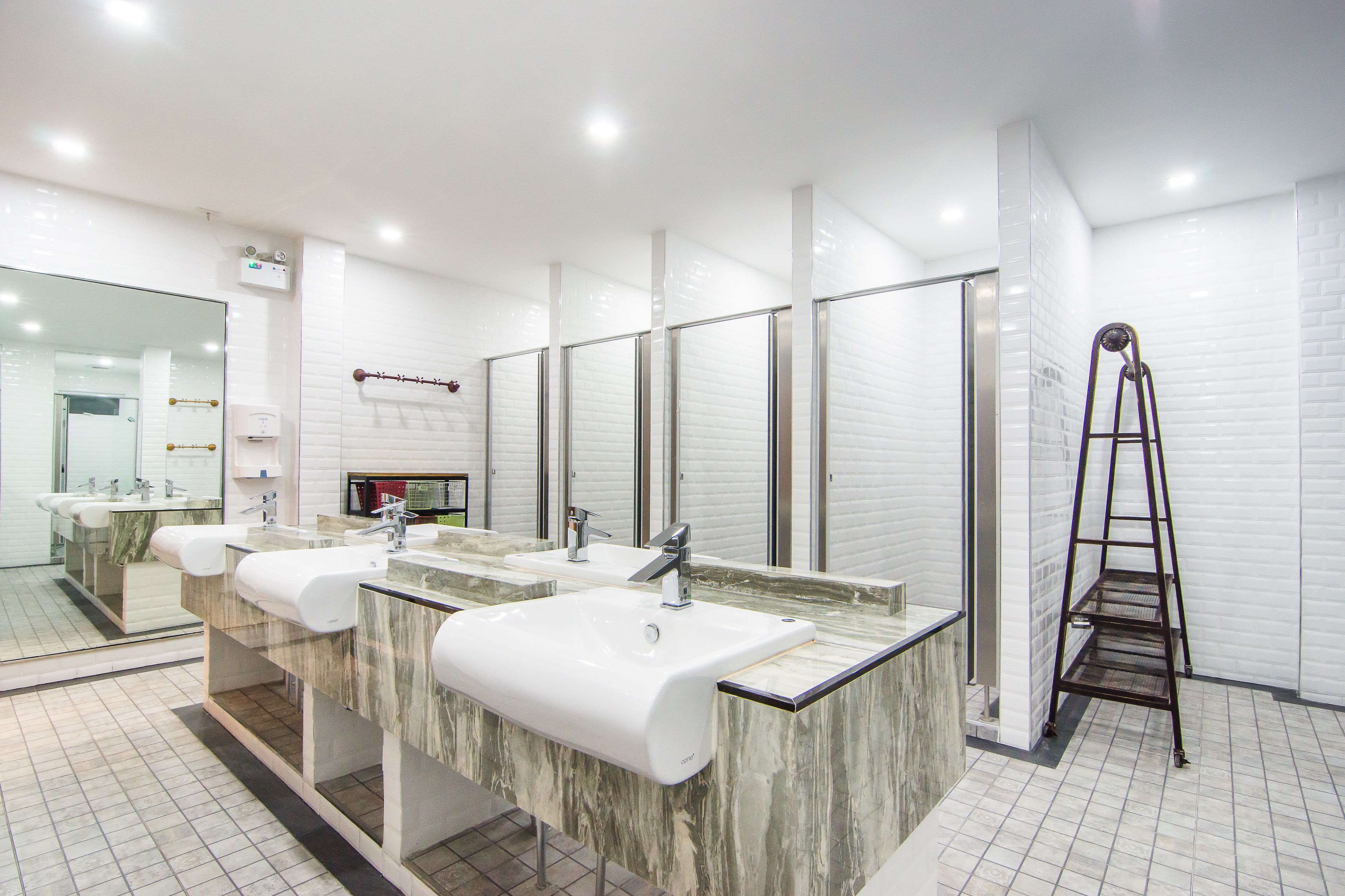 A modern bathroom with three sinks, a large mirror, and a ladder.