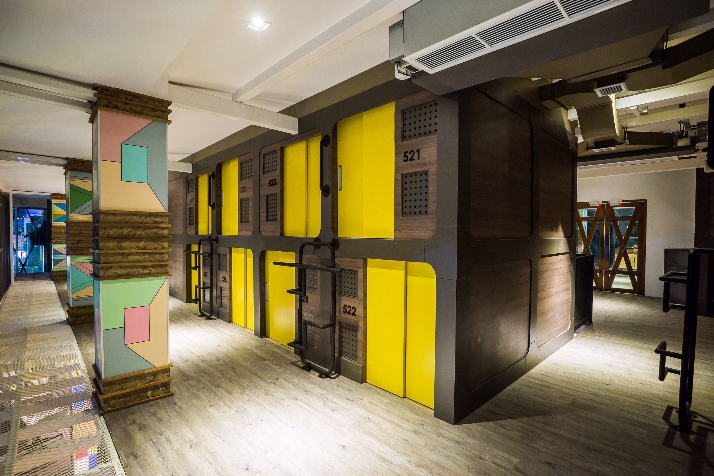 Interior moderno de hotel con un corredor central, taquillas amarillas y suelo de madera.