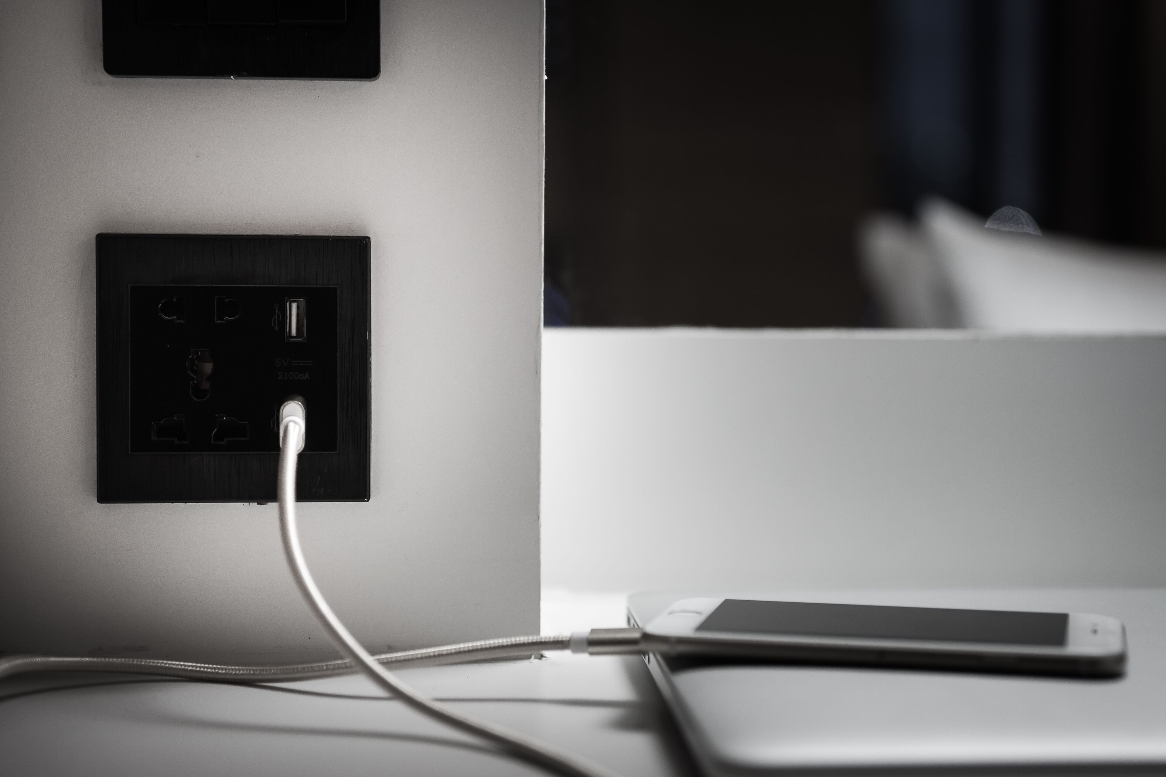 A smartphone connected to a power outlet on a white surface.