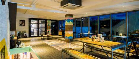 A modern interior with a wooden floor, a central table with benches, and a staircase leading to a balcony.