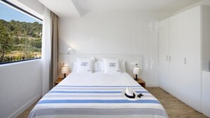 Een moderne hotelkamer met een groot bed, uitzicht op de omgeving en witte meubels.