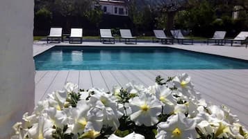 Une piscine entourée de fleurs blanches au premier plan, avec des chaises longues et une vue sur les montagnes en arrière-plan.