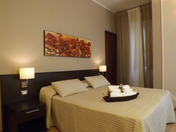 A hotel room with a bed, two bedside lamps, a nightstand, a wall-mounted painting, and a window with curtains. - La Maison des Rêves (Syracuse)