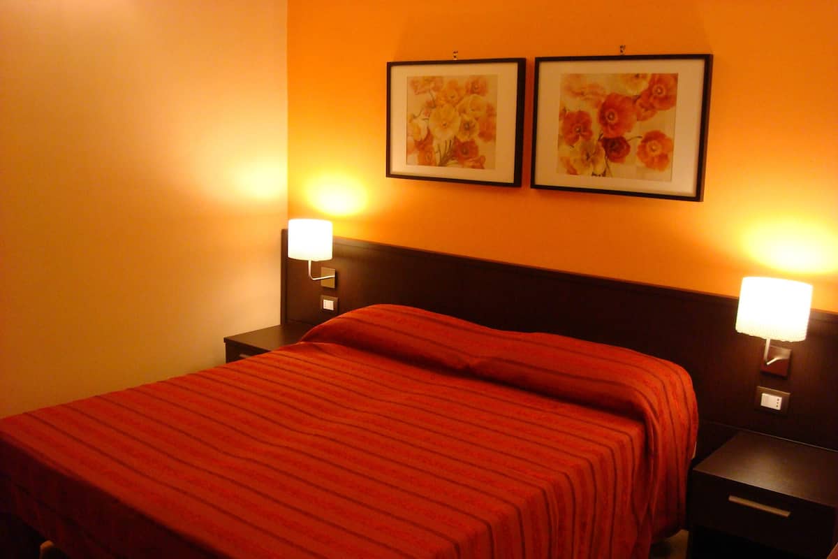A hotel room with a large bed, two bedside tables, and two wall-mounted lamps.