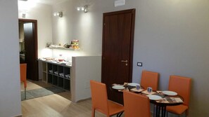 A dining area with a table set for four, orange chairs, and a wooden door. - La Maison des Rêves (Syracuse)