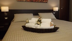 A hotel room with a bed, two bedside lamps, a floral artwork on the wall, and a tray with towels and flowers. - La Maison des Rêves (Syracuse)