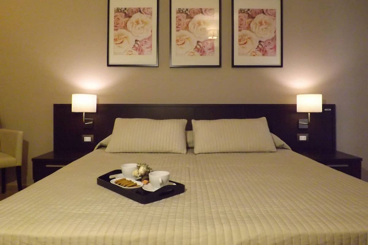 A neatly made bed with a tray of breakfast items, two bedside lamps, and three framed floral pictures on the wall.