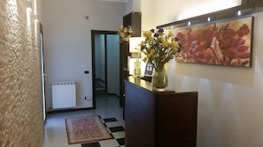 Un pasillo con un radiador, un tapete de cuadros, un florero con flores y un cuadro en la pared.