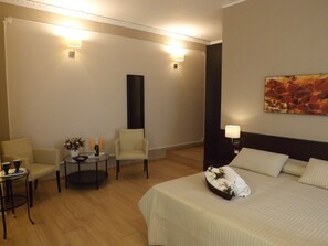 A hotel room with a bed, two armchairs, a small round table with a vase and wine bottle, and two wall-mounted lamps. - La Maison des Rêves (Syracuse)