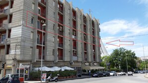 A multi-story building with balconies, a pizzeria, and parked cars. - La Maison des Rêves (Syracuse)