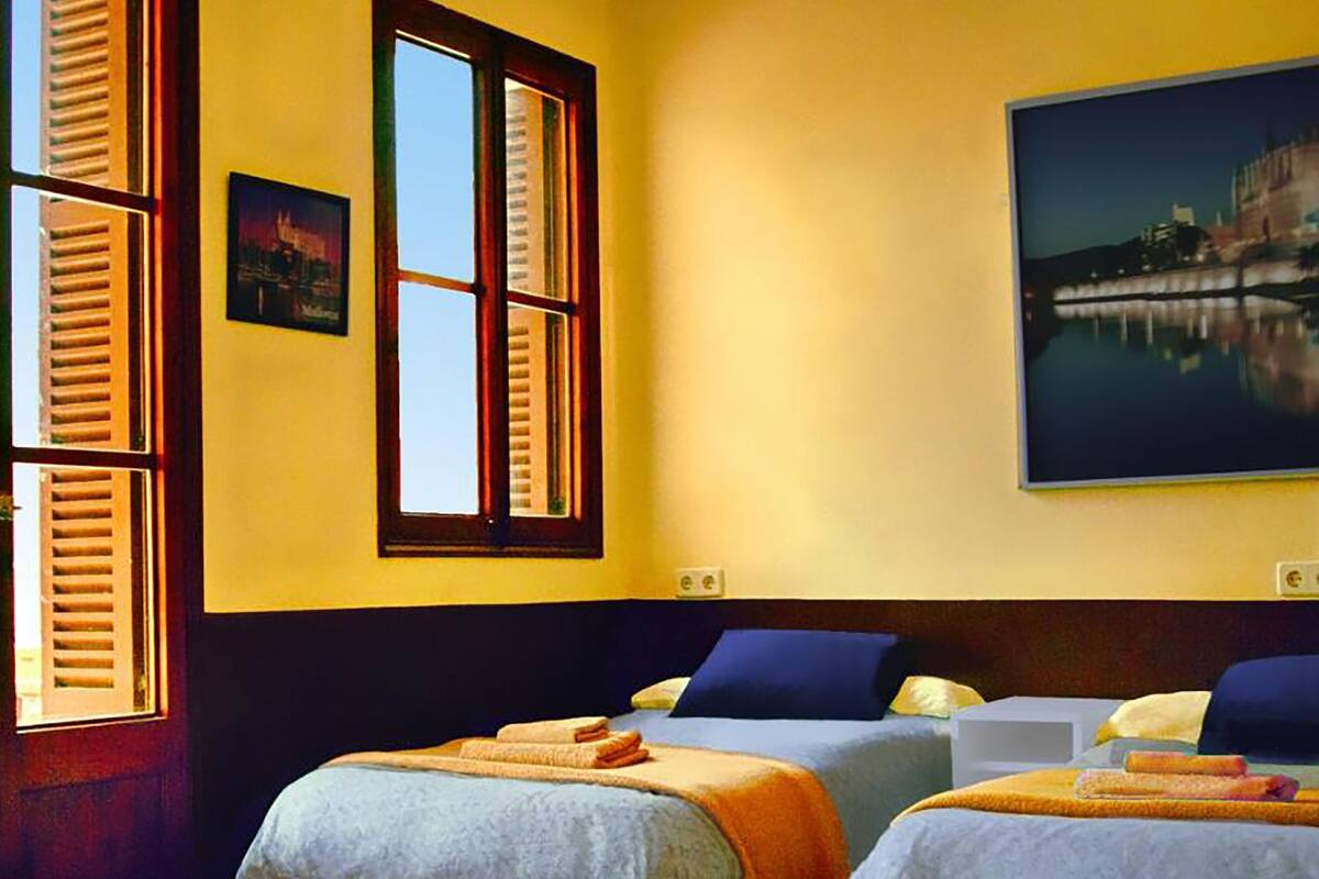 A hotel room with two beds, a large window with shutters, a painting of a cityscape, and a view of a body of water.