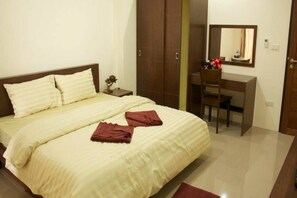 Quarto de hotel com cama, escrivaninha, cadeira, guarda-roupa e espelho.