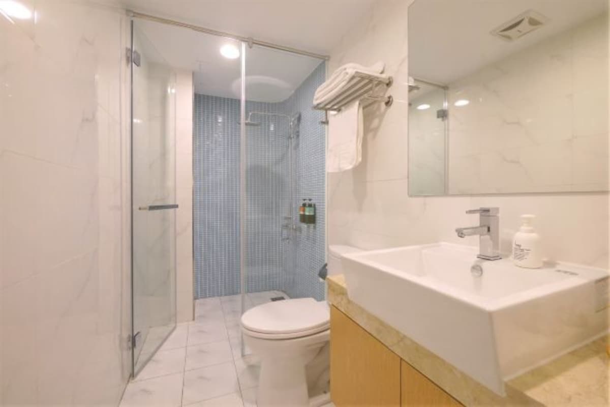 A modern bathroom with a glass-enclosed shower, a white toilet, and a large white sink with a mirror above it.