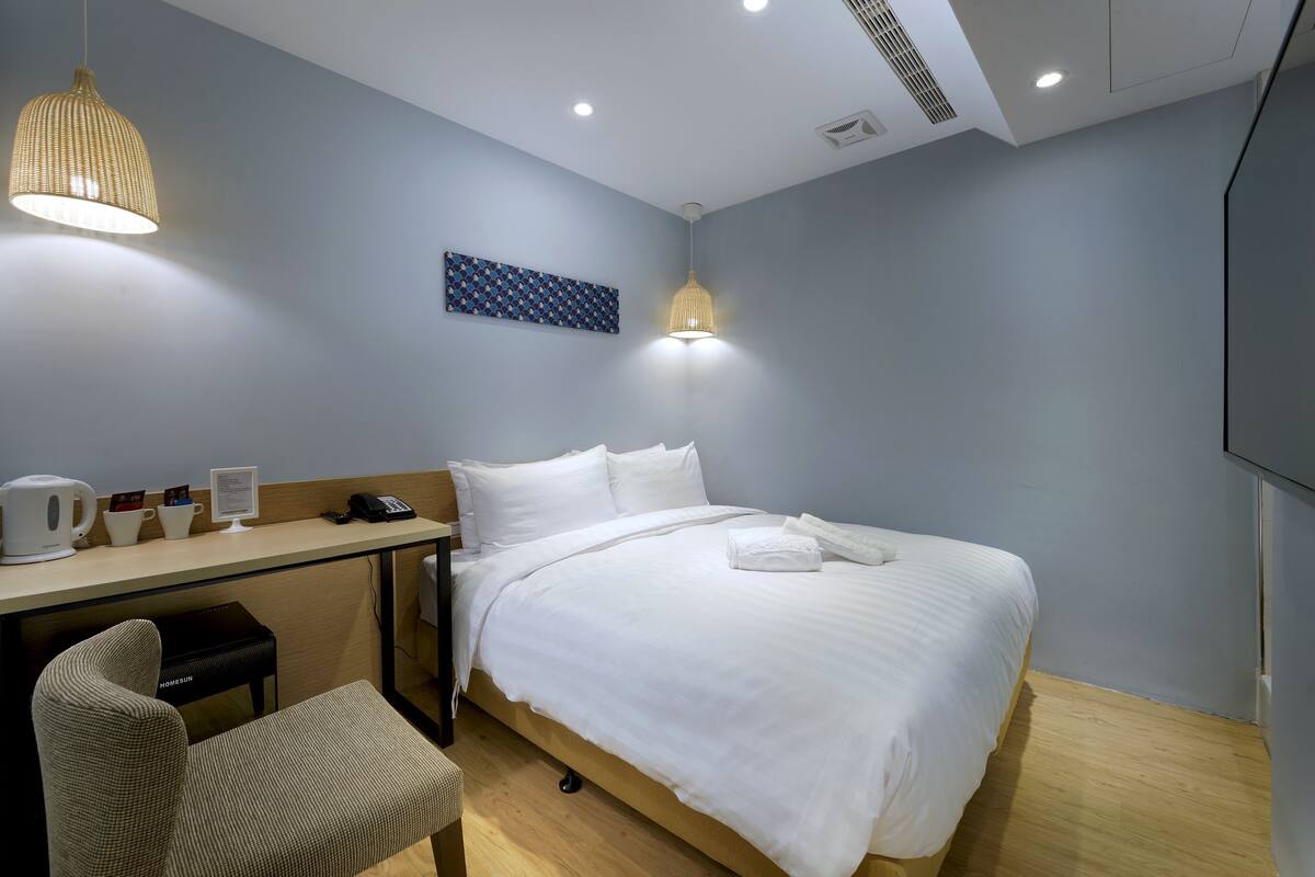 A hotel room with a bed, desk, chair, and a wall-mounted artwork.