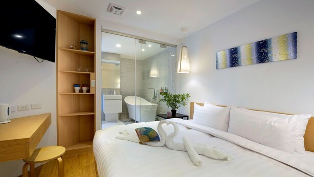 A hotel room with a bed, a wooden desk, a television, a glass shower enclosure, and a wall-mounted artwork. - SSBHotel - Shin Sei Bashi (Taichung)