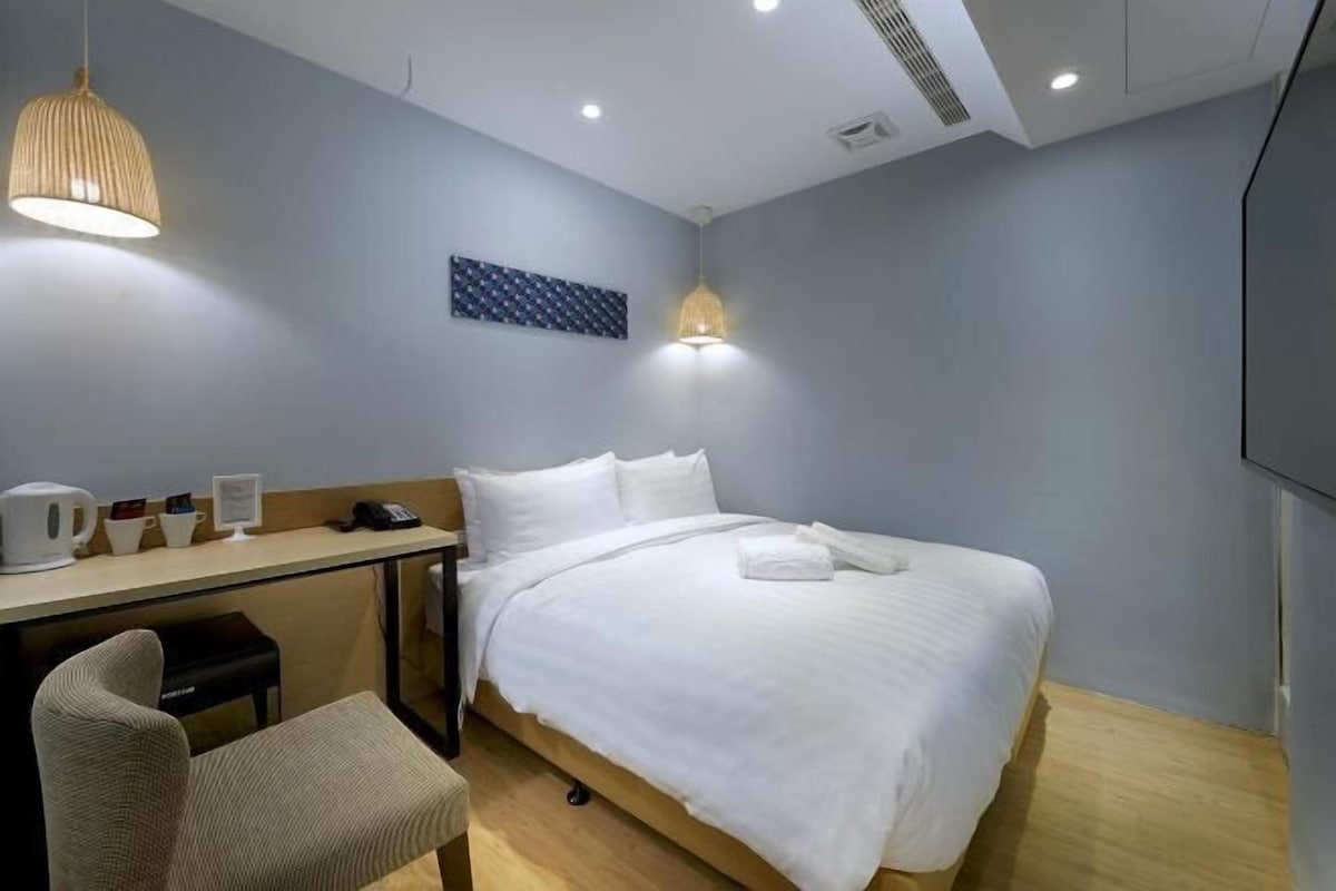 A hotel room with a bed, a desk, a chair, a coffee maker, and a TV.