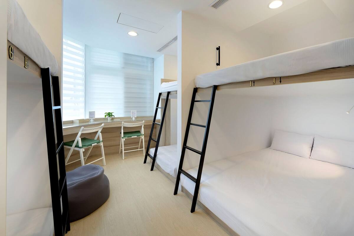 A bunk bed room with a desk and chair, a small potted plant, and a window with blinds.