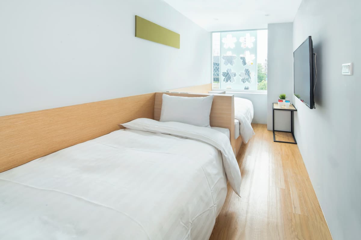 A modern hotel room with two beds, a TV, and a window with a city view.