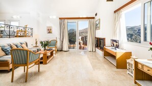 Een ruime woonkamer met een bank, stoelen, een televisie en een balkon met uitzicht op de bergen.