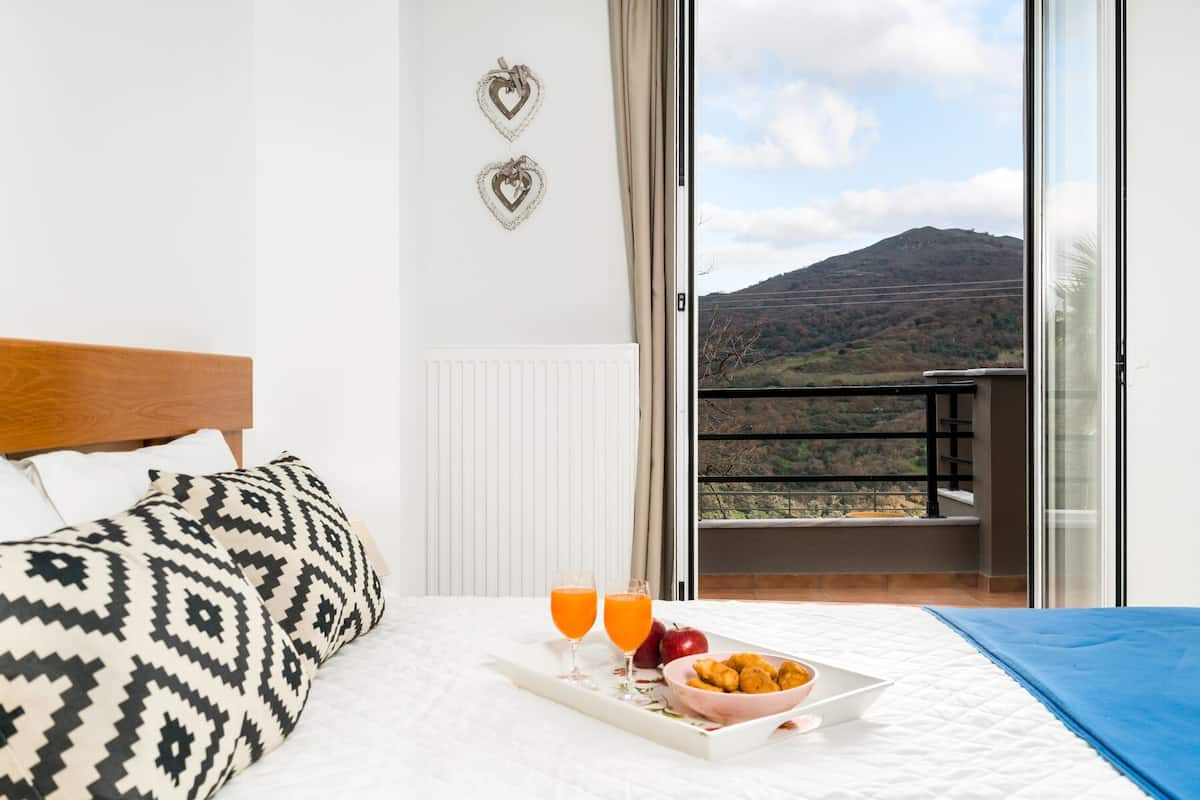 A hotel room with a bed, a breakfast tray with orange juice, and a view of a mountain.