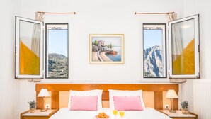 Een slaapkamer met een bed, twee nachtkastjes, een bijzettafeltje, een ingelijst beeld en een raam met gordijnen.