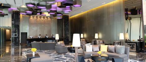 A modern lobby with geometric ceiling lights, plush seating, and a marble floor.