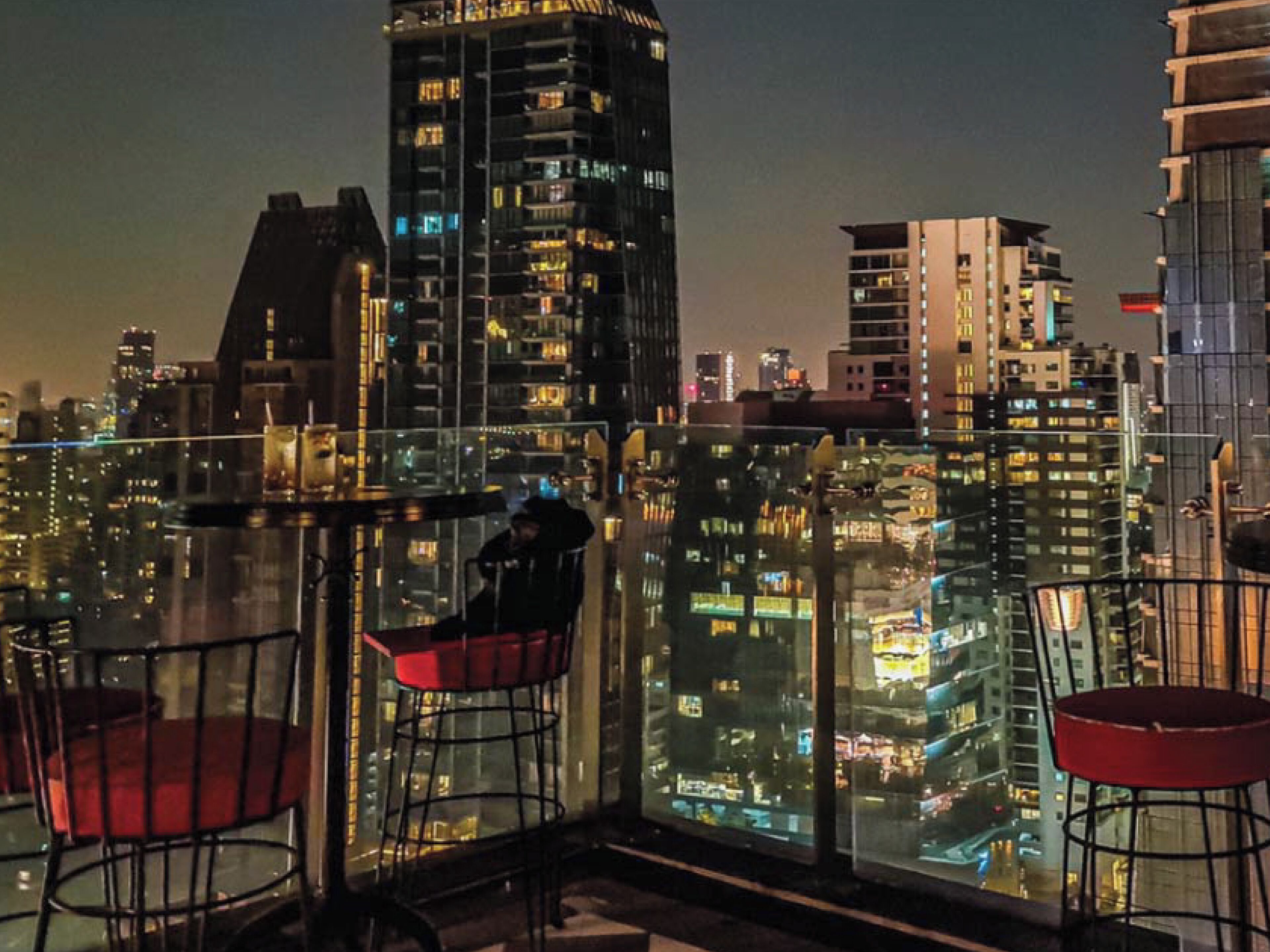 Um edifício alto com varanda de vidro e vista para a paisagem urbana à noite.