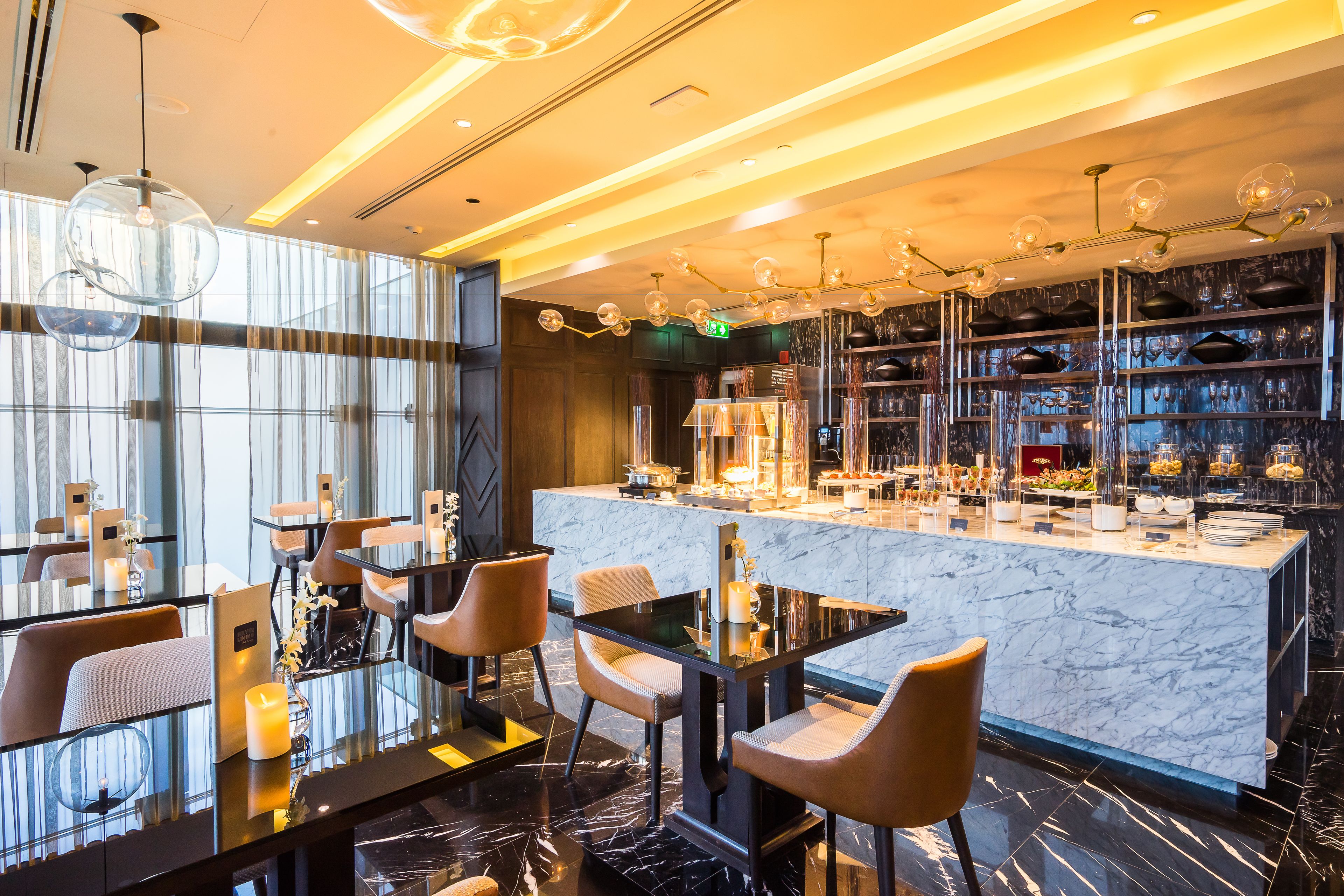 A modern restaurant with marble countertops, glass tables, and contemporary lighting fixtures.