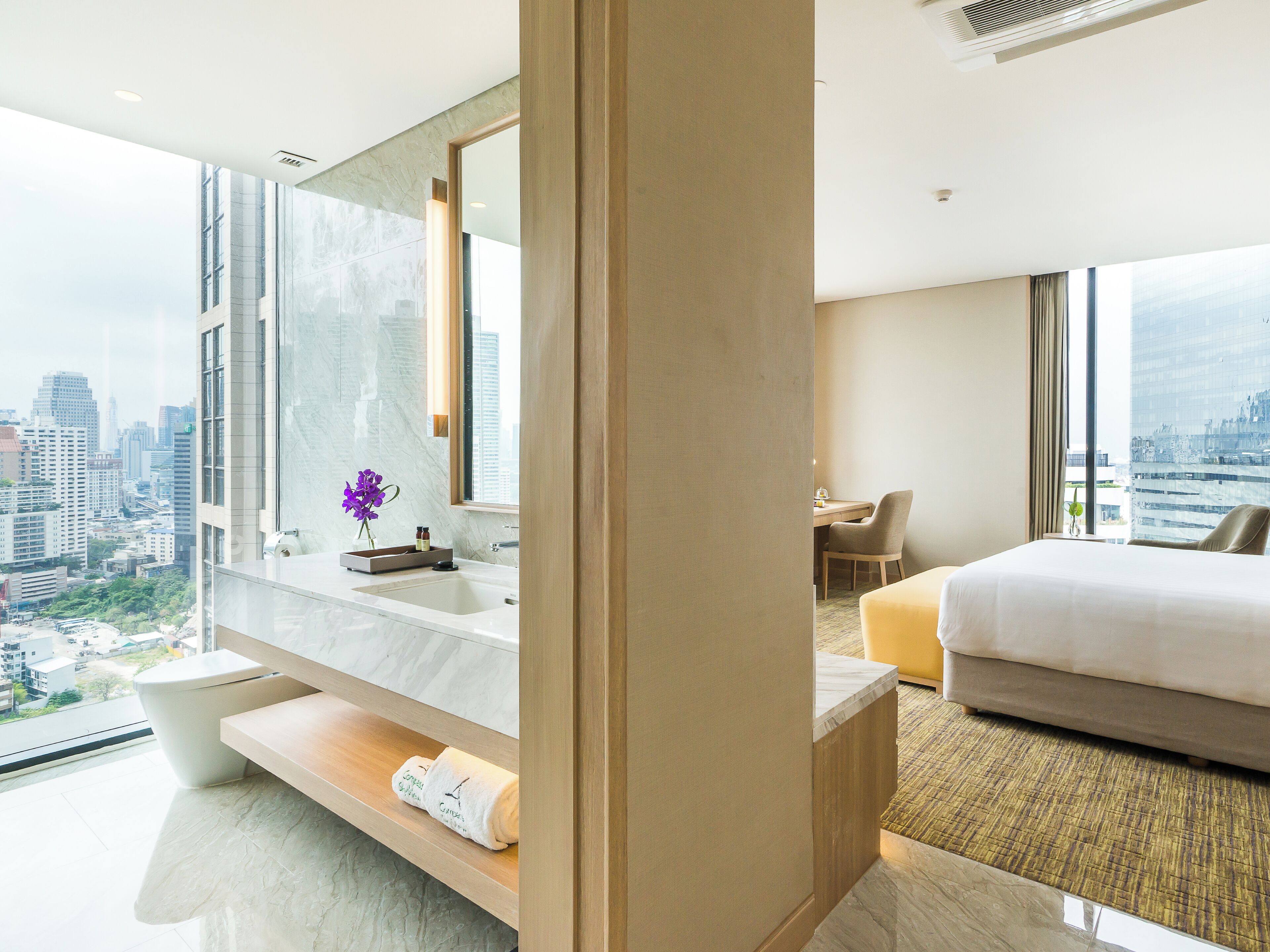 A modern hotel room with a large bed, a desk, and a bathroom with a marble vanity.