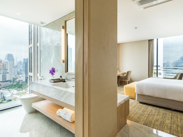 Una habitación de hotel moderna con una cama grande, un escritorio y un baño con tocador de mármol.