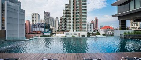 A rooftop pool with lounge chairs, surrounded by high-rise buildings and a clear sky.