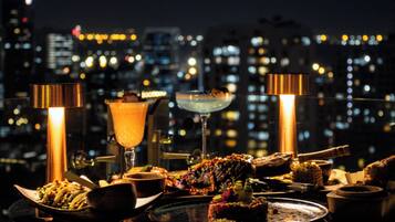 Una mesa servida con diversos platos y bebidas, con un paisaje urbano de fondo.