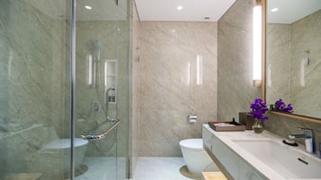 A modern bathroom with a glass-enclosed shower, a marble-tiled wall, a white toilet, and a vanity with a mirror.