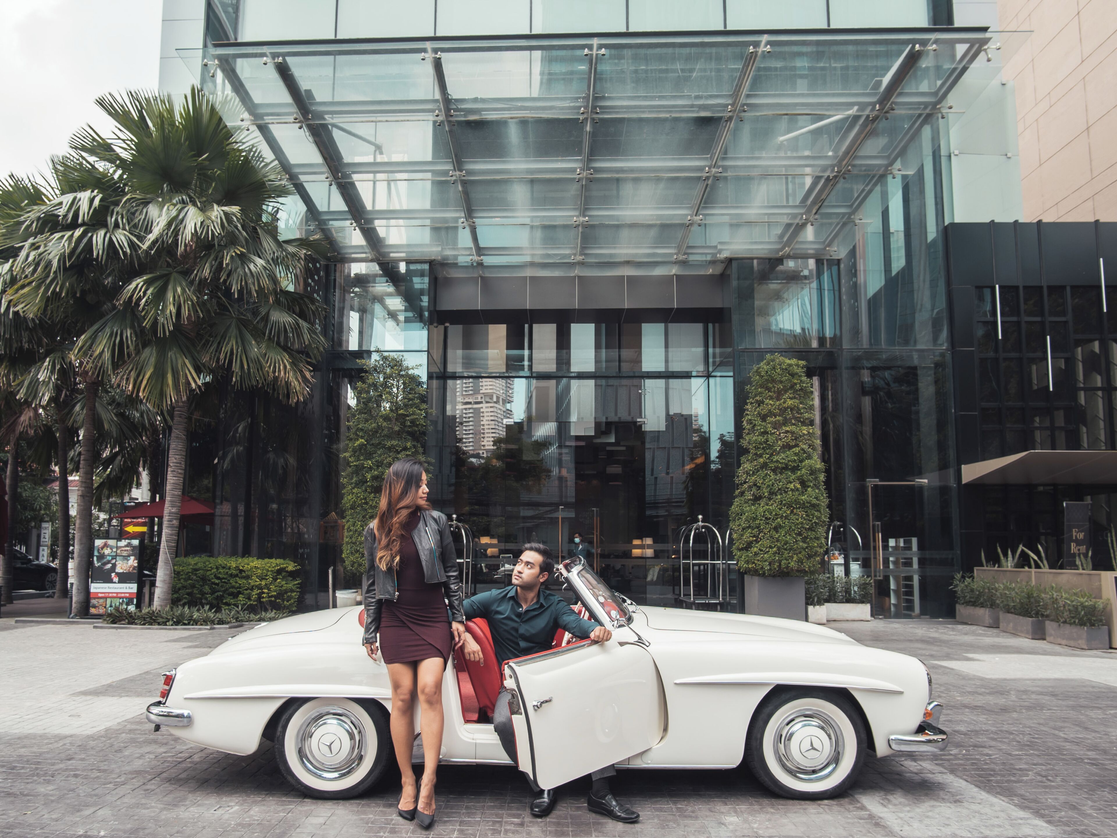 A white convertible car parked in front of a modern building with glass and metal architecture.