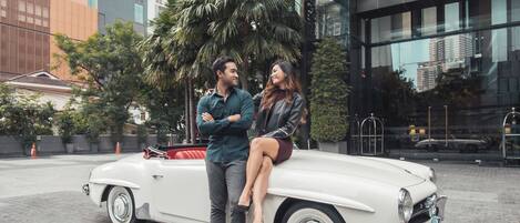 Un coche descapotable clásico aparcado frente a un edificio moderno con ventanas de cristal y una palmera.