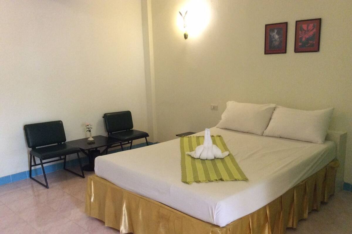 Une chambre d’hôtel avec un lit, deux chaises, une petite table et une lampe fixée au mur.
