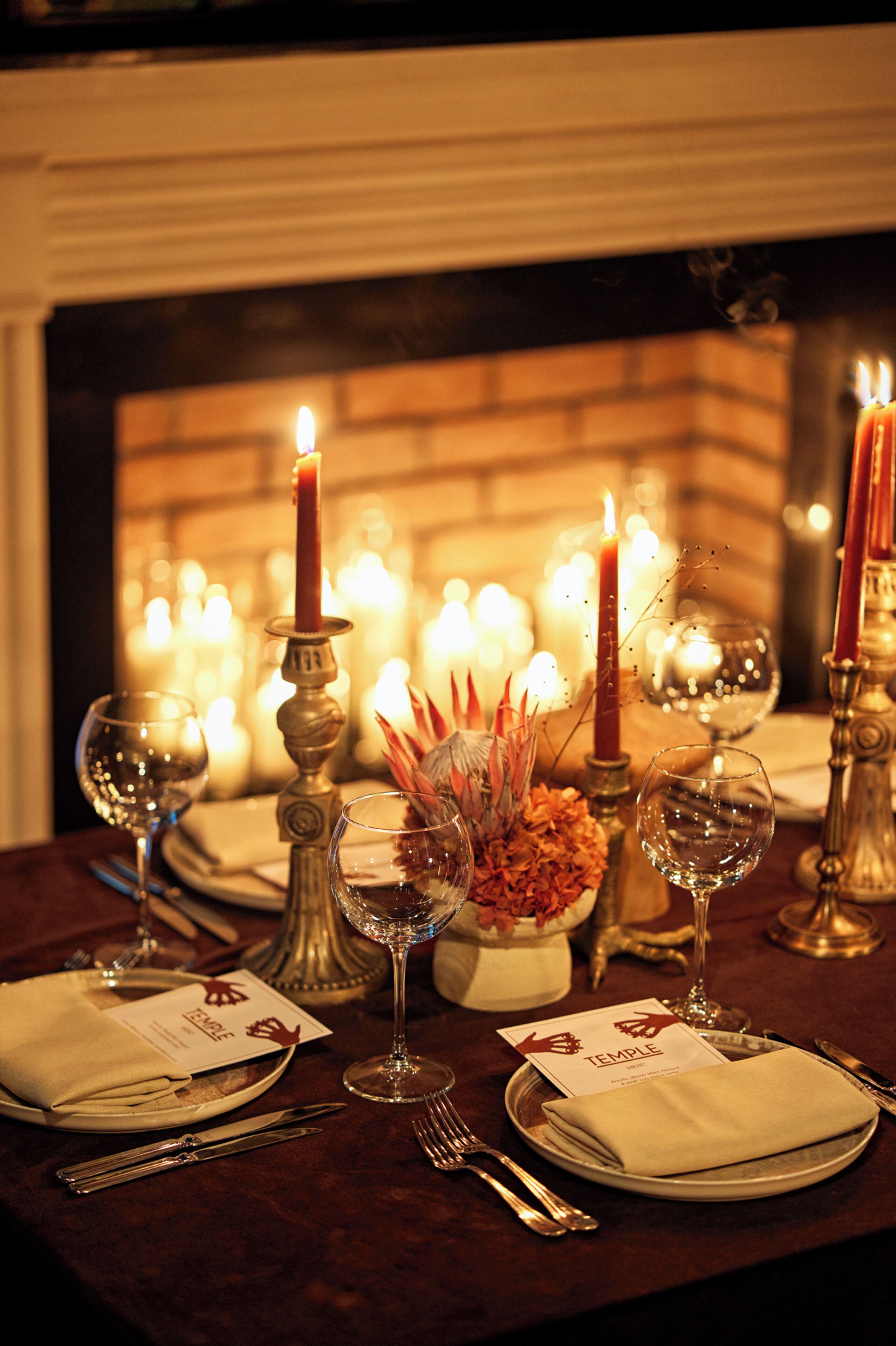 A dining table set for a meal with candles, glasses, and a menu.