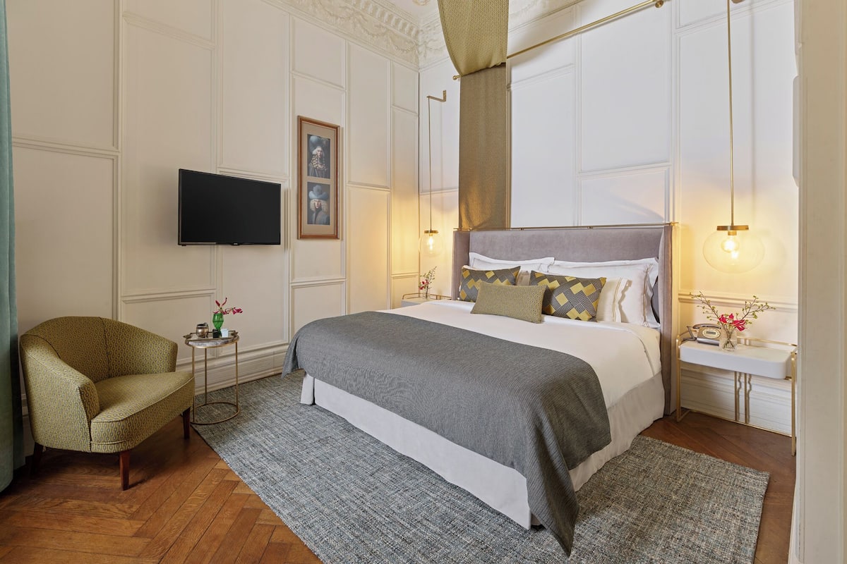 A hotel room with a bed, a television, a chair, a bedside table, and a nightstand.