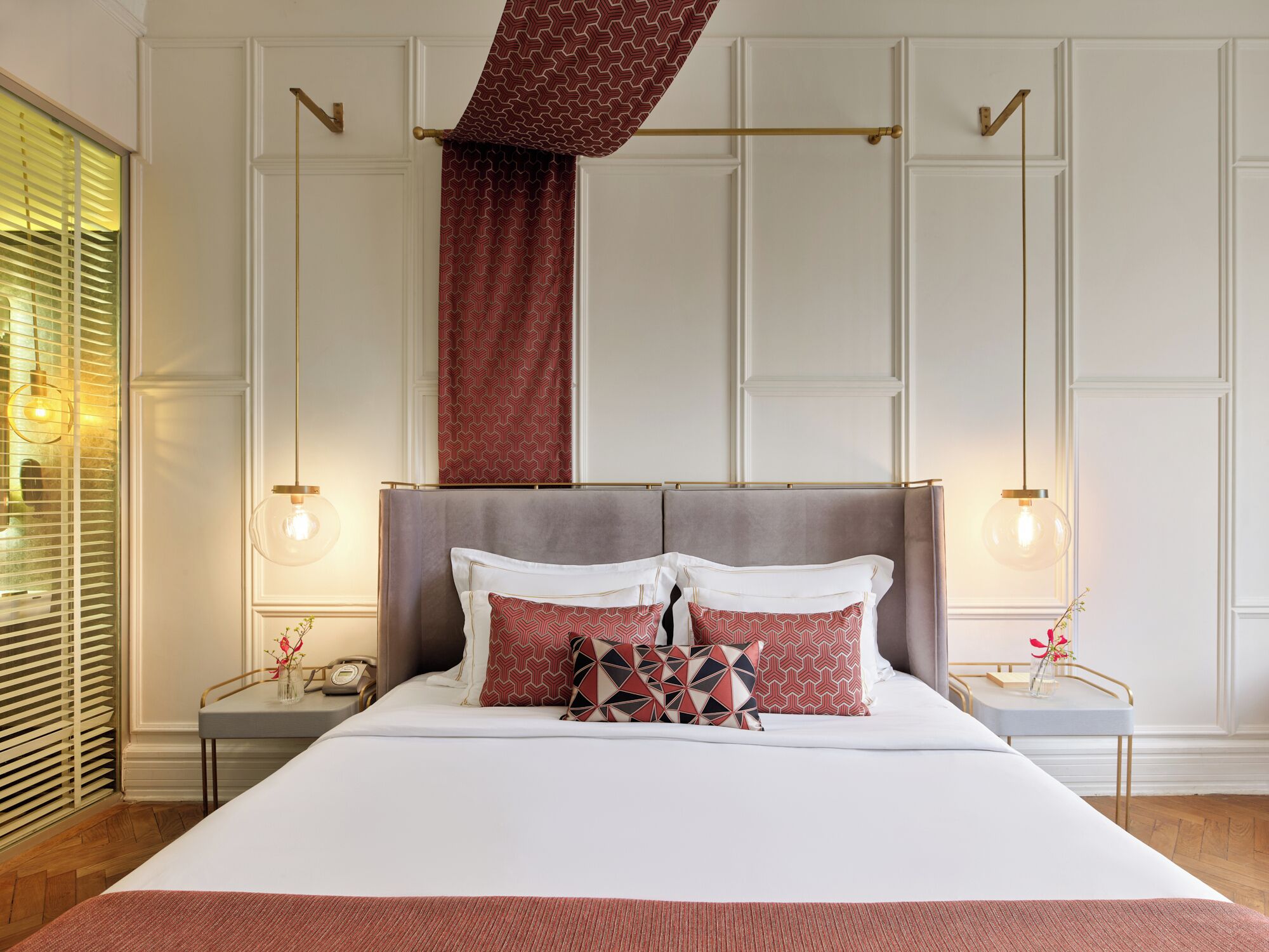 Une chambre d’hôtel avec un grand lit, deux tables de chevet, une tête de lit et une fenêtre avec des stores.