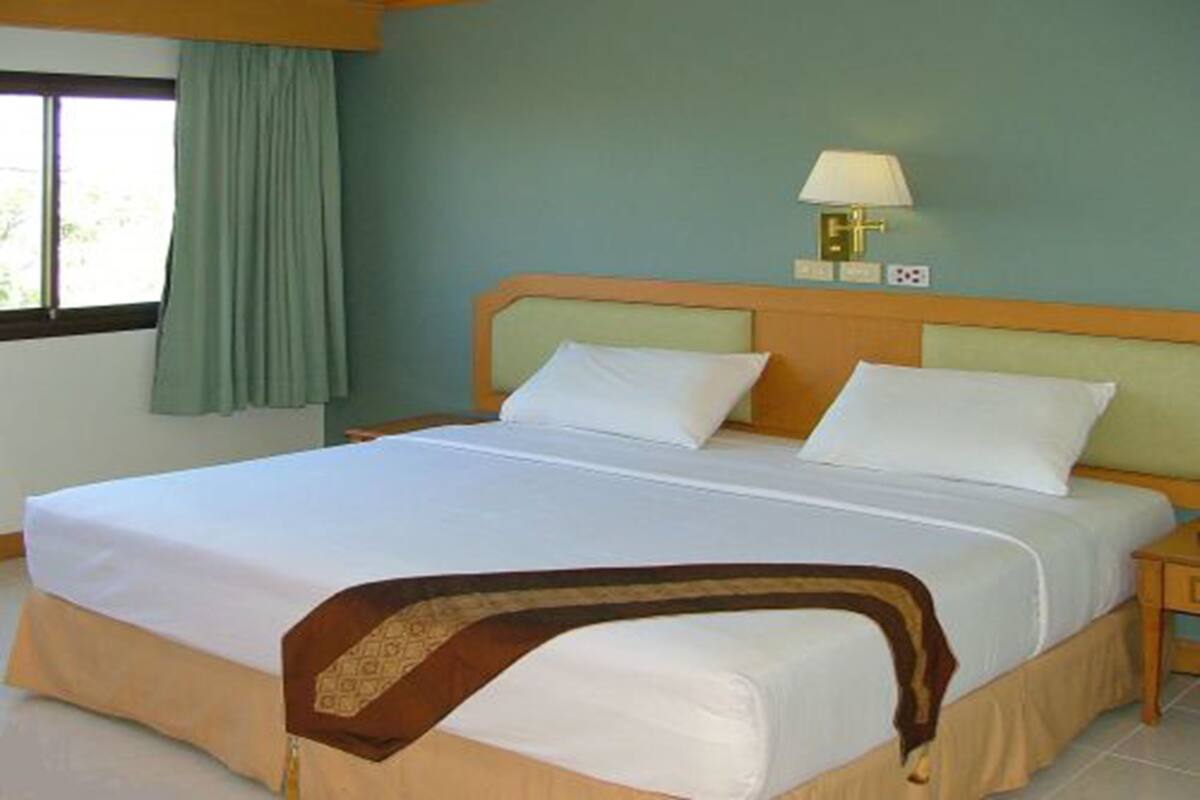 Ein Hotelzimmer mit einem großen Bett, einem Nachttisch, einer Lampe und einem Fenster mit Vorhängen.