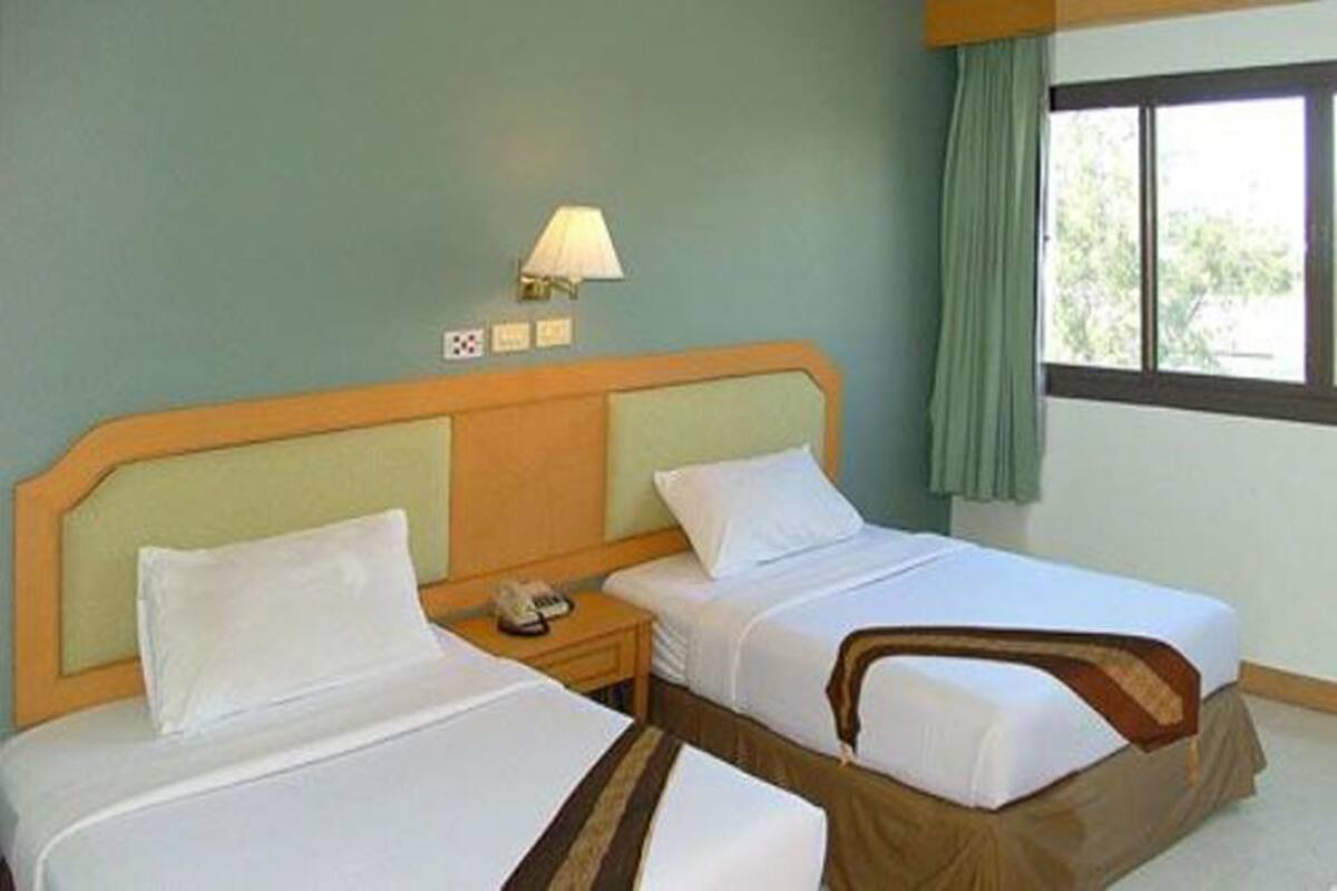 Ein Hotelzimmer mit zwei Betten, einem Nachttisch mit Lampe und einem Fenster mit Vorhängen.