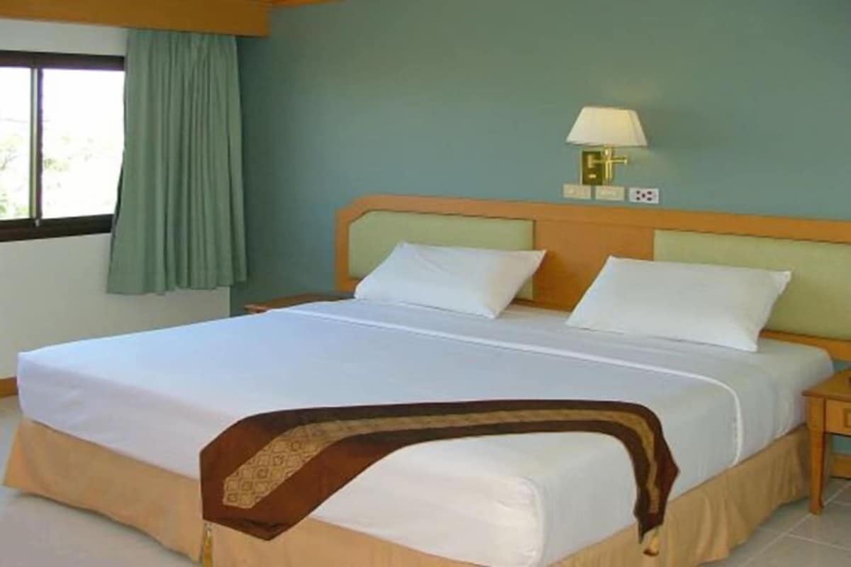 A hotel room with a bed, a nightstand, a lamp, and a window with curtains.