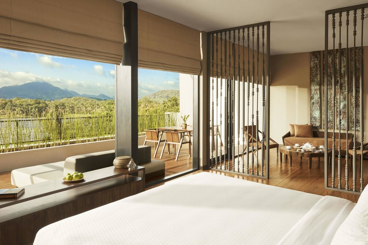 A modern hotel room with a large bed, a balcony with a view of mountains, and a dining area with a table and chairs.