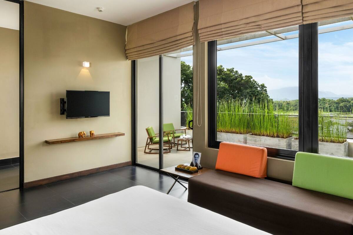 A modern hotel room with a large window, a flat-screen TV, a sofa, and a small table with a picture frame.
