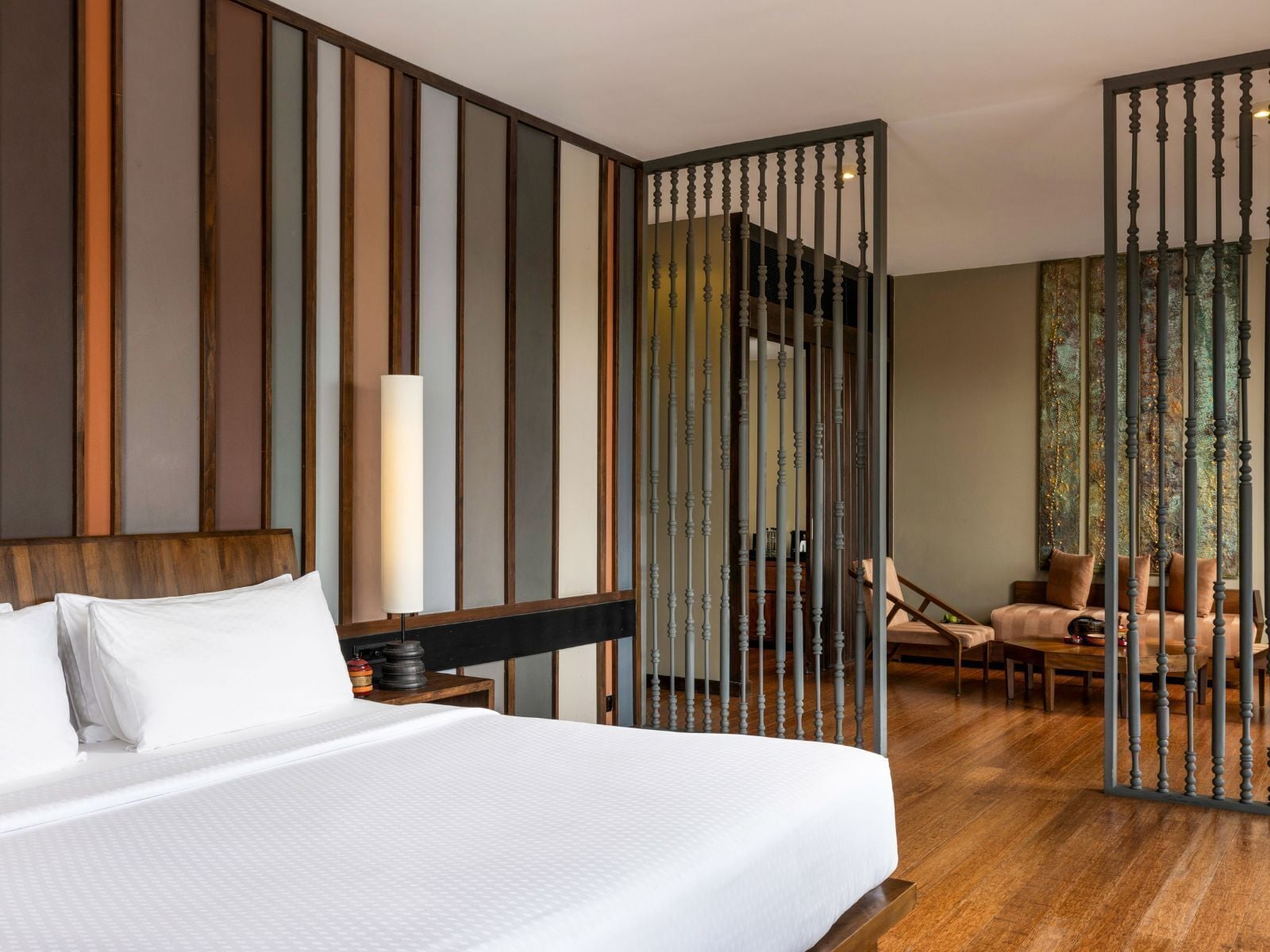 A hotel room with a large bed, a wooden headboard, a nightstand, a desk, a chair, and a decorative wall panel.