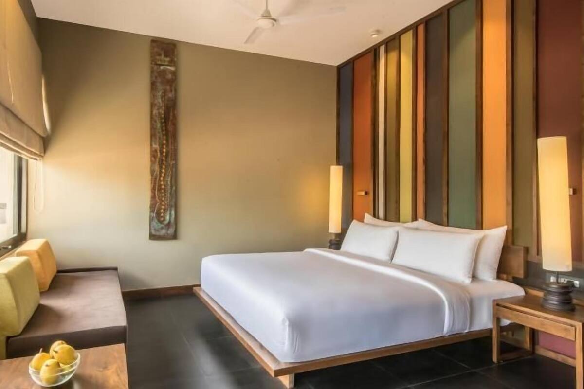 A hotel room with a bed, bedside tables, a small table with lemons, a wall art piece, and a window.
