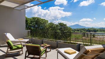 Un balcón con sillones de descanso y una mesa, con vistas a un paisaje exuberante y montañas.
