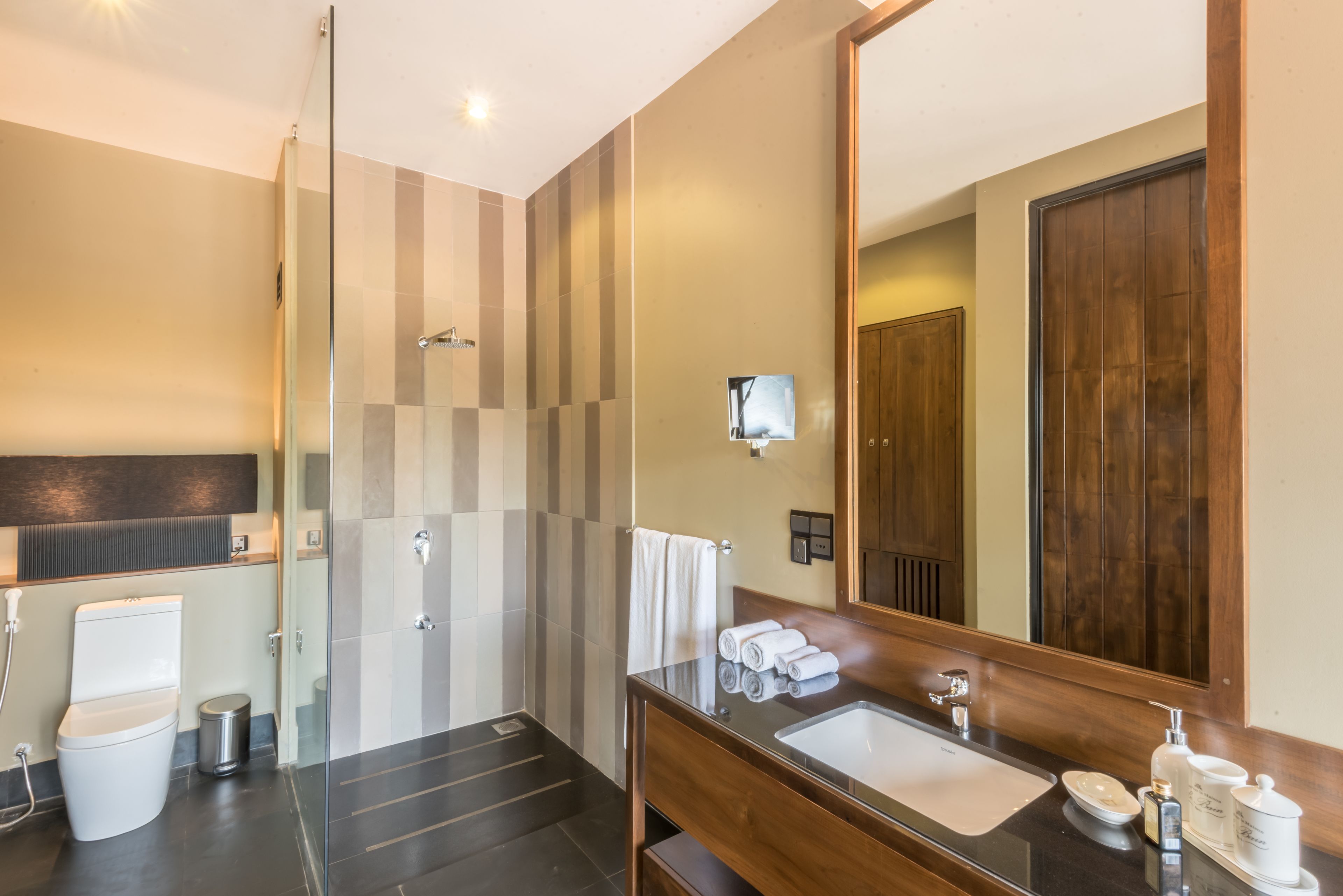 A modern bathroom with a glass shower enclosure, a wooden vanity with a sink, and a large mirror.
