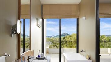 A modern bathroom with a large bathtub, a vanity with a mirror, and a view of a mountainous landscape through large windows.